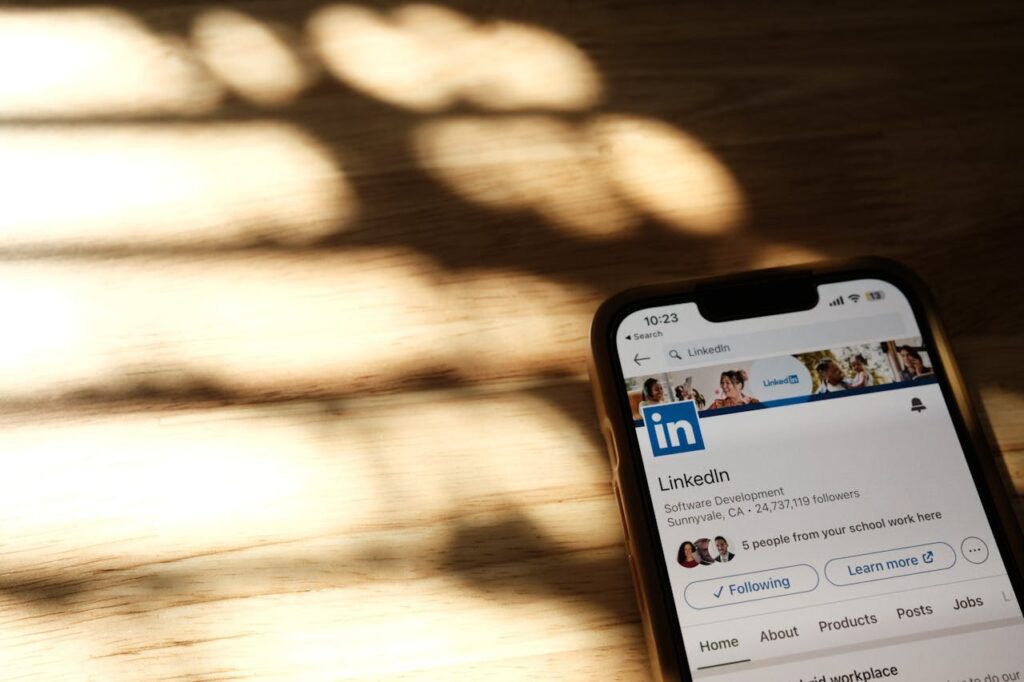 Close-up of a smartphone showing a LinkedIn profile page on a wooden table with shadows.